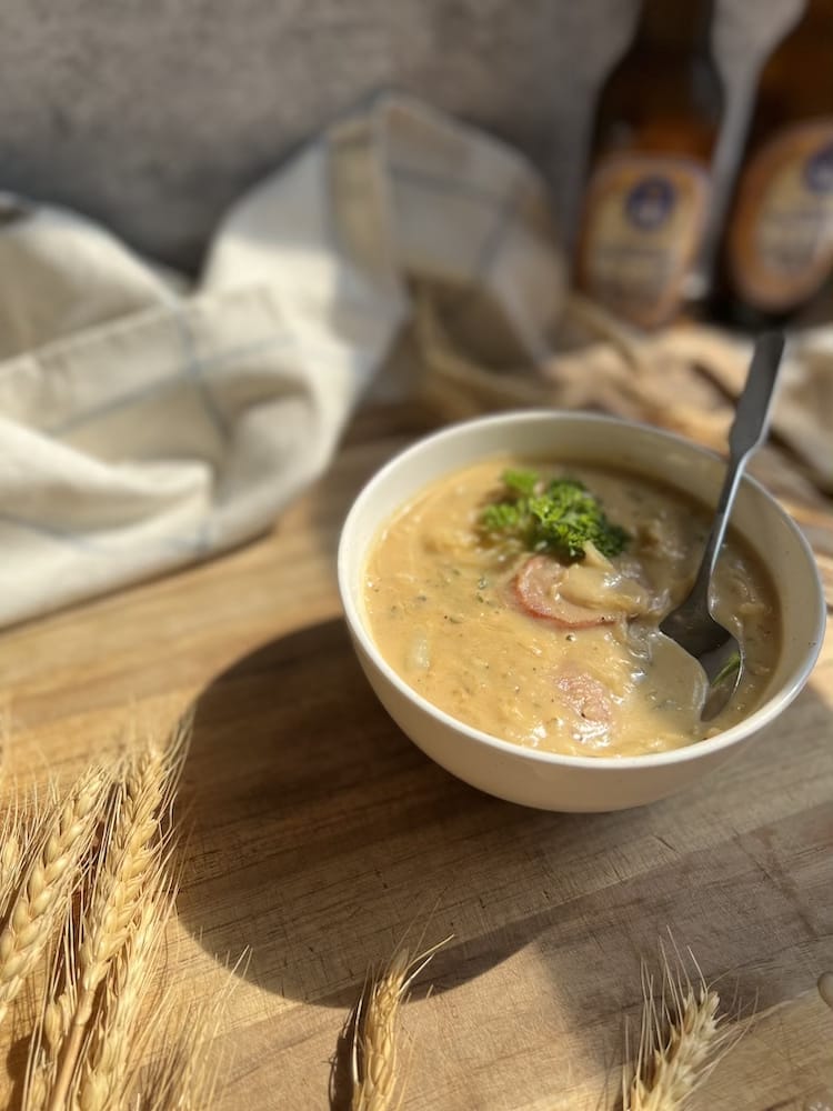 Creamy Kielbasa Sauerkraut Soup on a wooden cutting board with beer bottles in the background