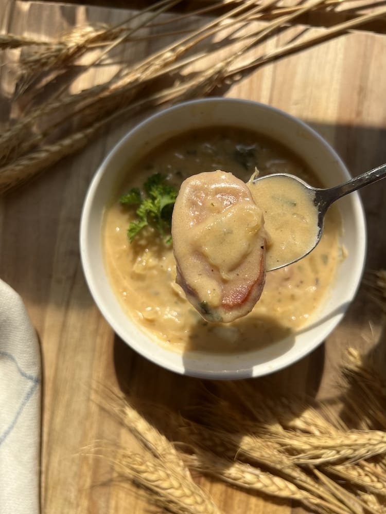 Creamy Kielbasa Sauerkraut Soup with spoon showing slice of kielbasa