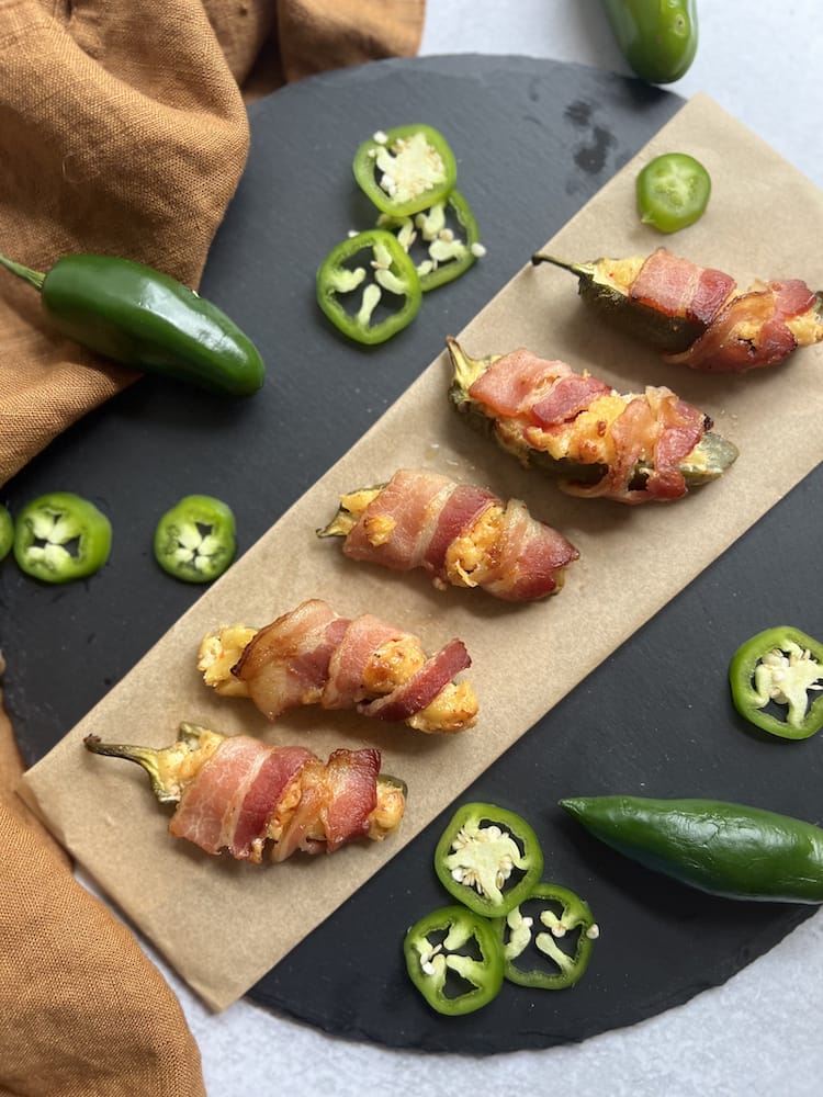 Bacon Wrapped Pineapple Jalapeño Poppers on parchment paper surrounded by sliced jalapeños