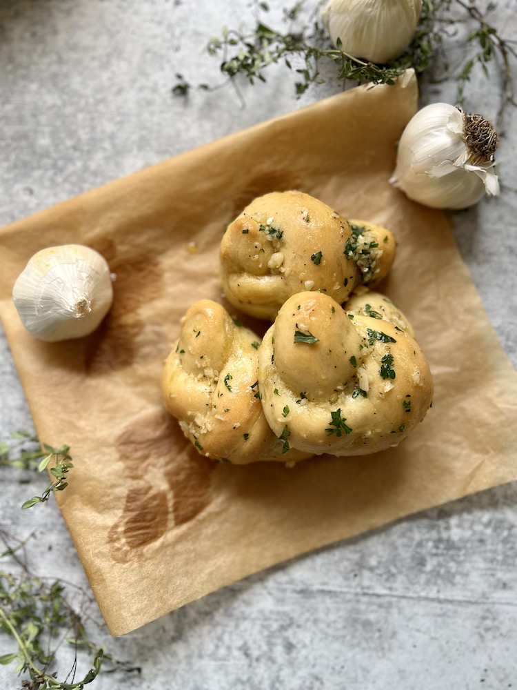 Homemade Garlic Knots on parchment paper with two heads of garlic