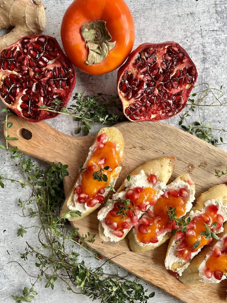 Pomegranate Persimmon Crostini arranged on a small wooden cutting board