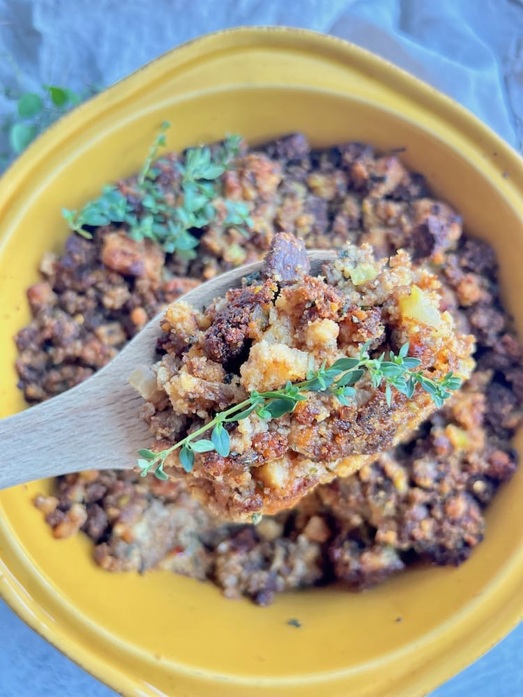 Pumpernickel Cornbread Stuffing with Sausage in a baking dish with wooden spoon