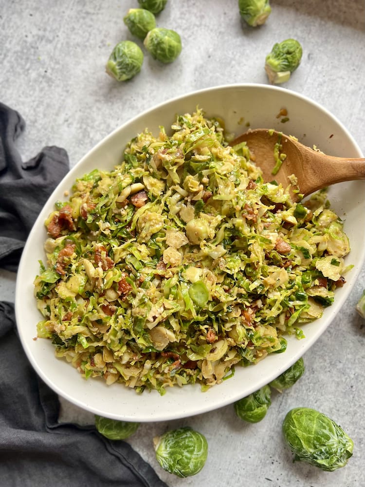 Sauteed Brussels Sprouts with Bacon in a serving dish with wooden spoon