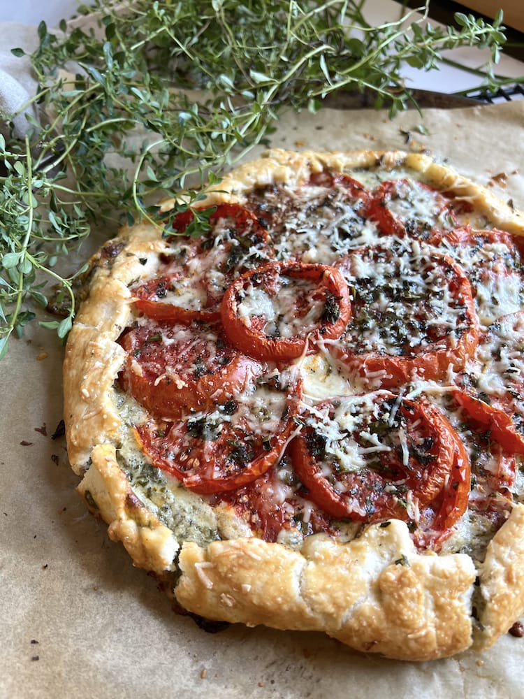 Tomato Galette on parchment paper next to fresh thyme and oregano