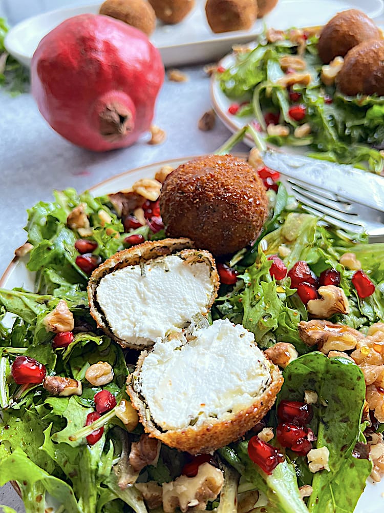 Fried Goat Cheese Salad with one goat cheese ball slice open over bed of spring mix, pomegranate seeds, and chopped walnuts