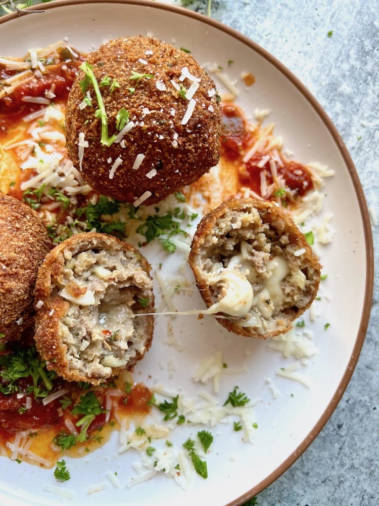 Italian Fried Meatballs on a plate with one meatball sliced in half to reveal gooey mozzarella cheese