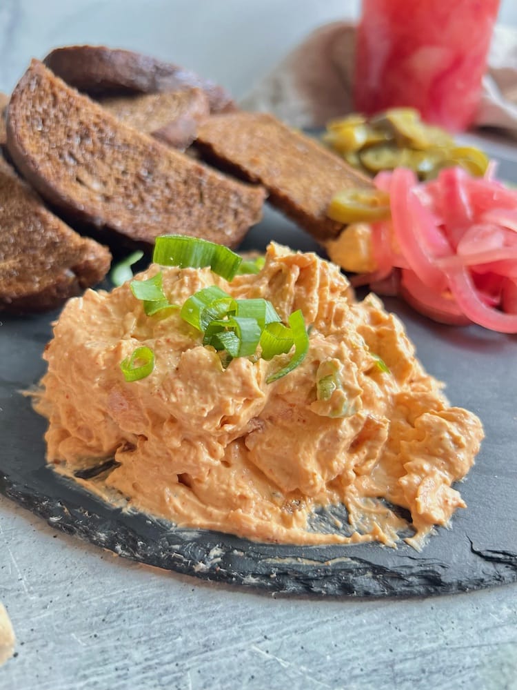 Smoked Trout Dip on serving board with pumpernickel ciabatta, pickled onions, and pickled jalapeños