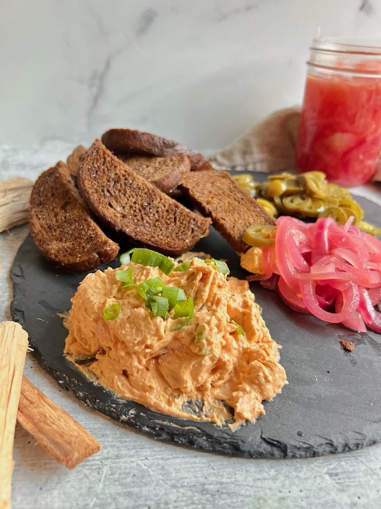 Smoked Trout Dip on a black serving platter with pumpernickel crostini and pickled onions and jalapeños