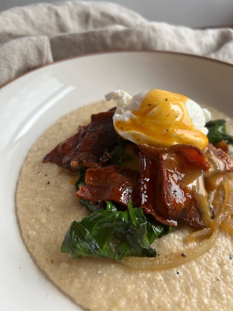 Breakfast Grits with Pepper Jelly Bacon on a plate with sautéed onions and wilted spinach.