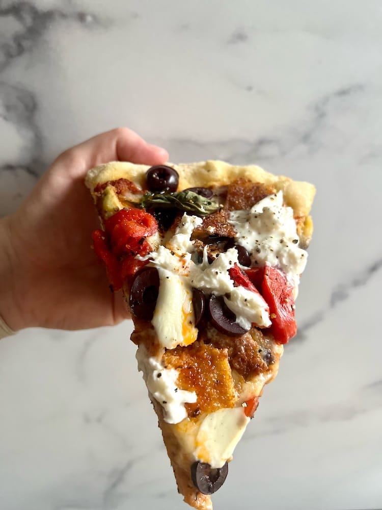 A slice of Fried Eggplant PIzza held in the air