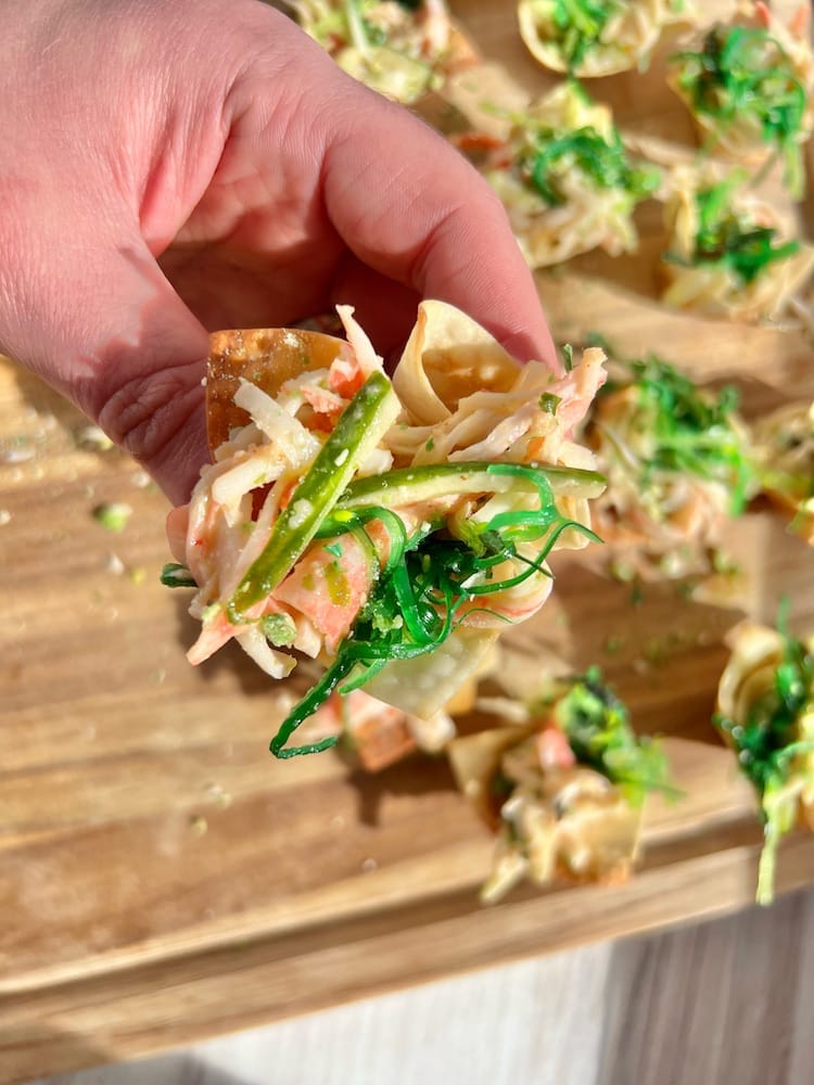Kani Salad Bite held in hand with more Kani Salad Bites below on cutting board