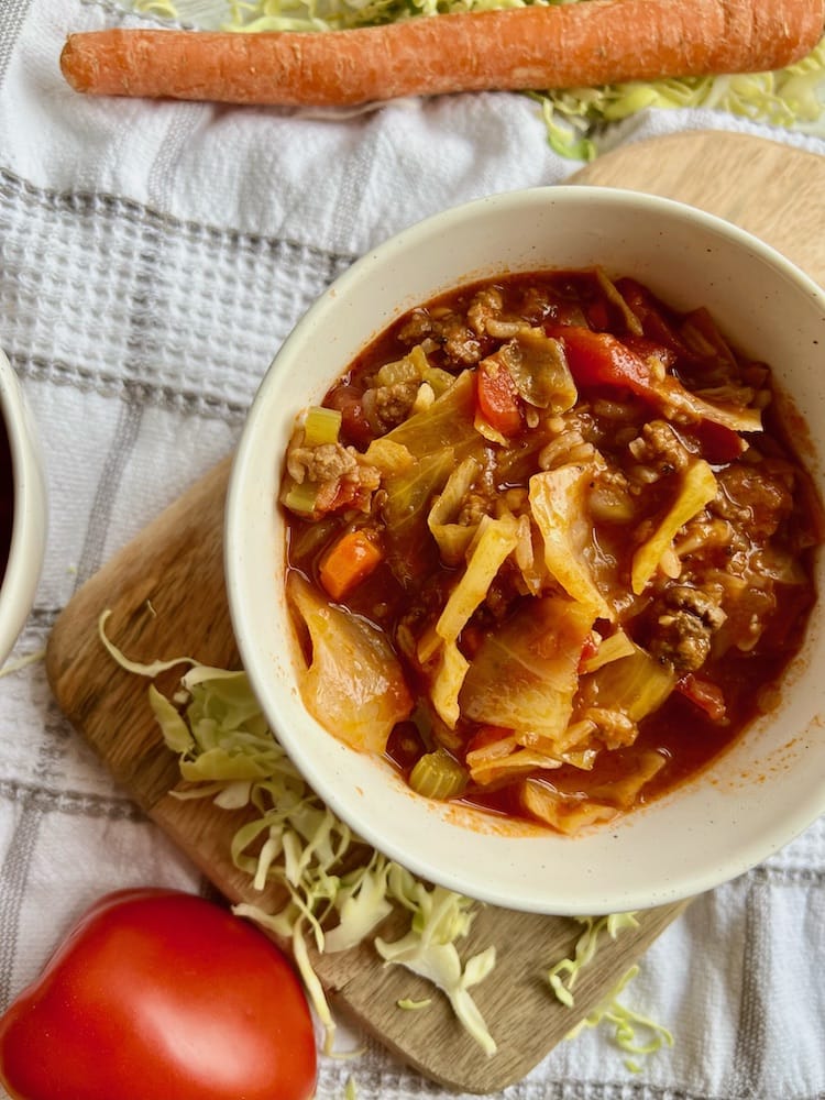 Old-Fashioned Cabbage Soup in a bowl next to a tomato and carrot