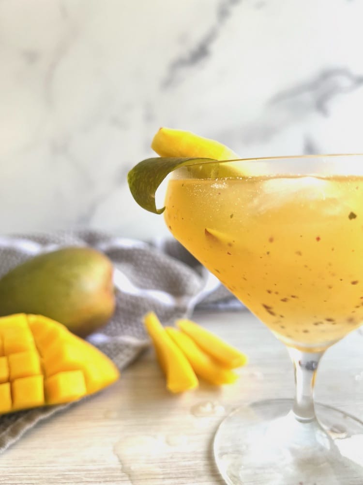 Peppercorn Mango Margarita in a short-stemmed Margarita glass with fresh mango in the background