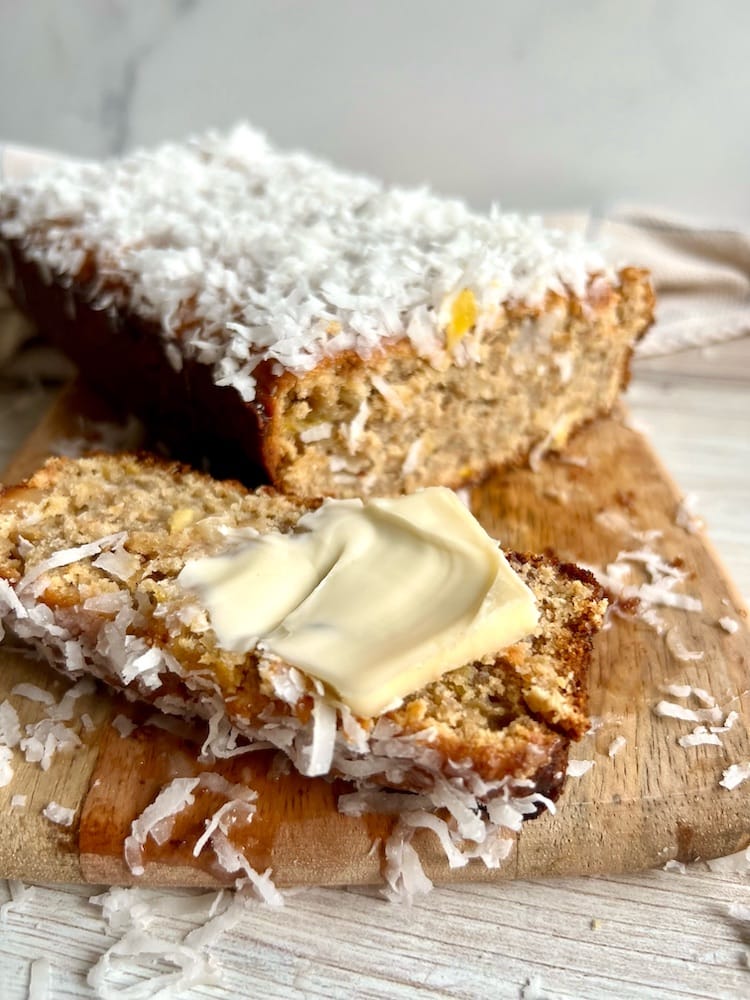 Piña Colada Banana Bread on a cutting board with one slice laying down with butter pat on it