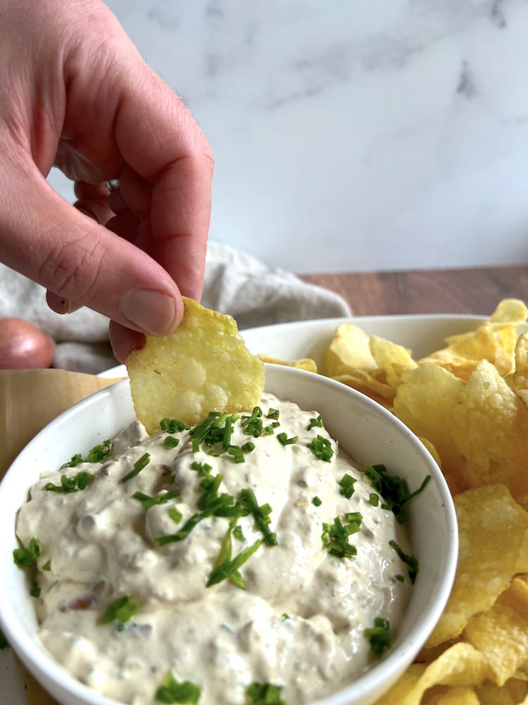 Sour Cream and Onion Dip in a bowl with a chip being dipped into it