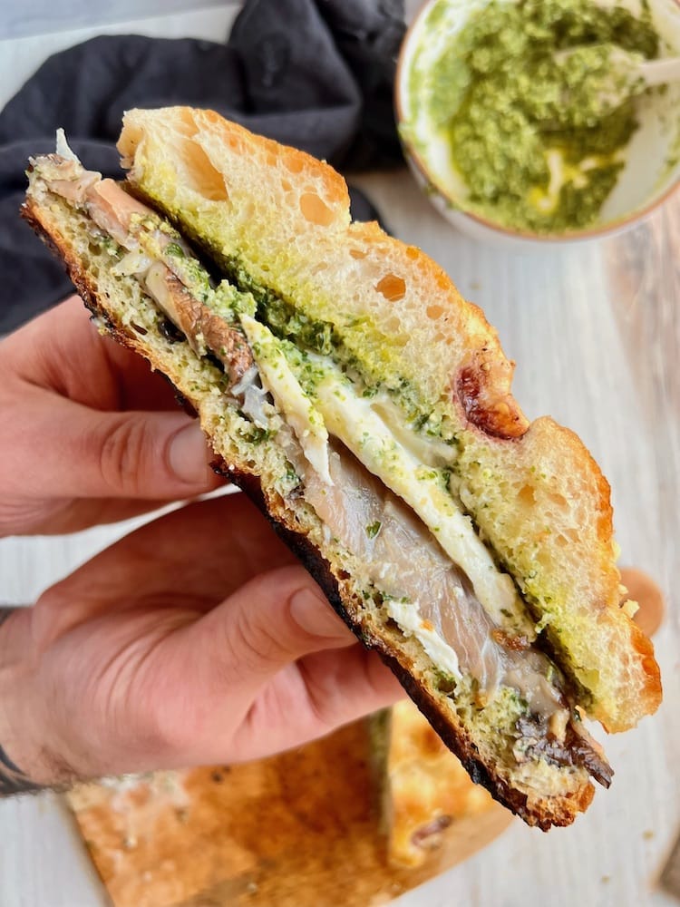 A Mushroom Sandwich with Arugula Pesto sliced in half and sliced side shown to the viewer
