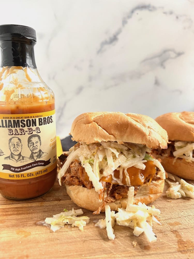 Two Pulled Pork Jicama Slaw Sandwiches next to a bottle of BBQ sauce