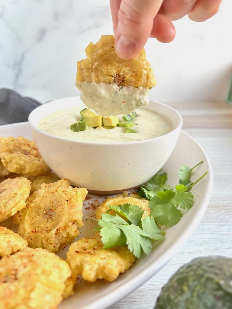 Tostones with Spicy Avocado Ranch Dip with a hand holding one tostone in the dip.
