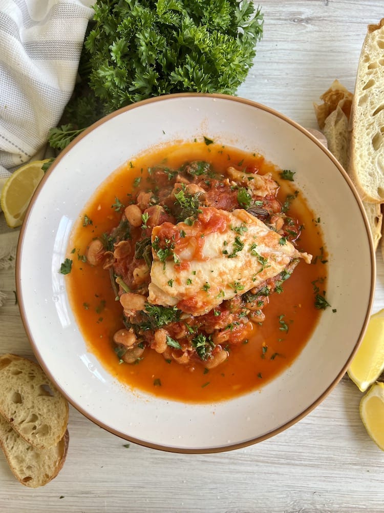 Tuscan Fish Stew in a pasta bowl surrounded by bread slices and fresh parsley