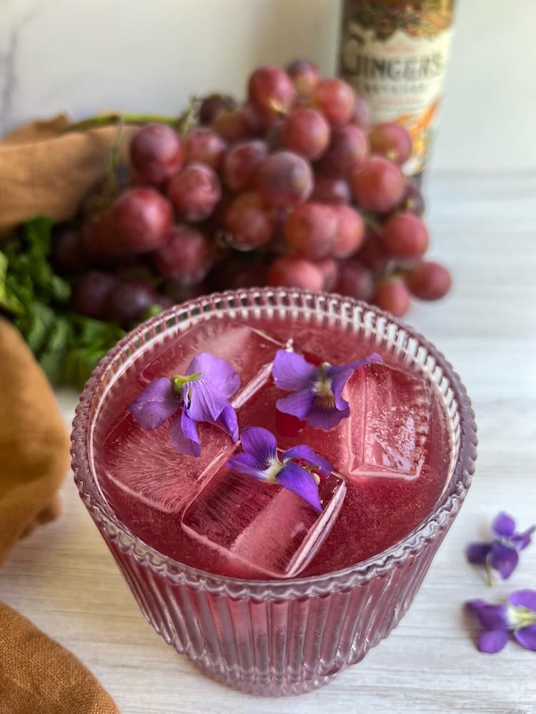 The Yankee Transfusion Cocktail in a rocks glass with ice and a grape bunch behind it