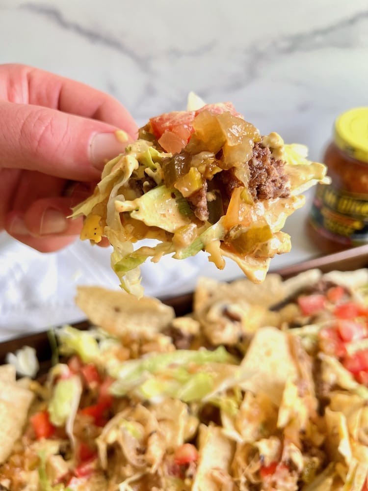 Cheeseburger Nachos with Mac Sauce with one loaded chip being held toward the viewer