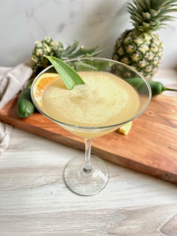 A Pineapple Martini next to a cutting board with a pineapple on it