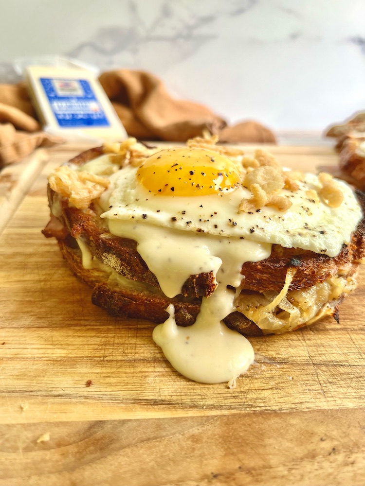 Hangry Croque Madame on a cutting board with block of gruyere cheese in background