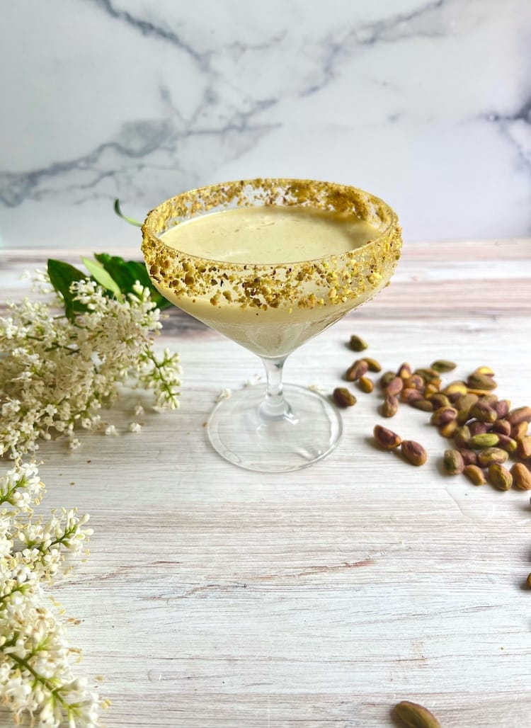 A Pistachio Martini next to white tiny flowers and roasted pistachio