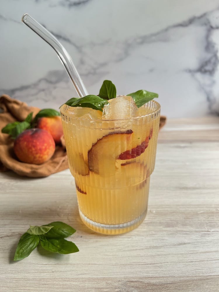 Peach Basil Gin and Tonic in a rocks glass with peach slices and basil sprig