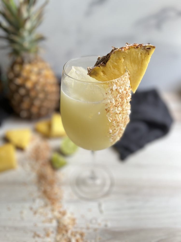 Piña Colada Sangria in a stemmed wine glass with pineapple wedge as garnish