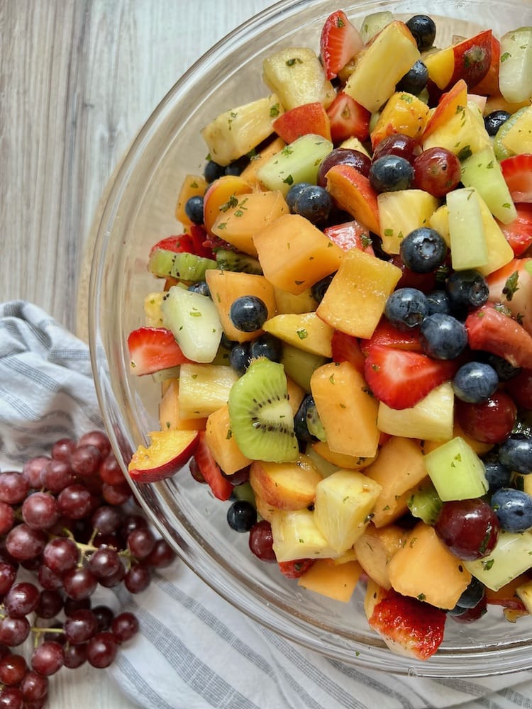 Summer Fruit Salad in a large serving bowl next to a bunch of grapes