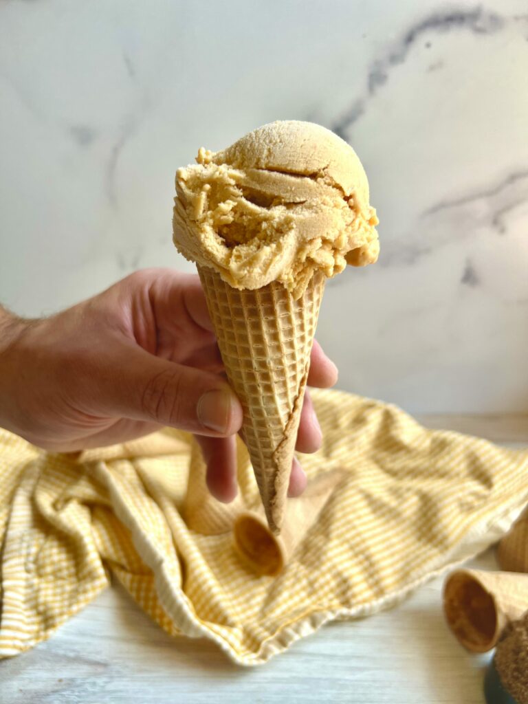 Brown Sugar Apricot Ice Cream on a waffle cone with a hand holding it
