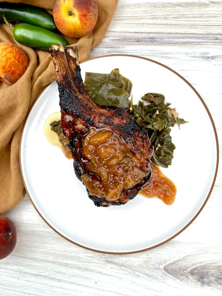A Grilled Double Cut Pork Chop on a plate topped with peach jalapeño chutney and a bed of collard greens