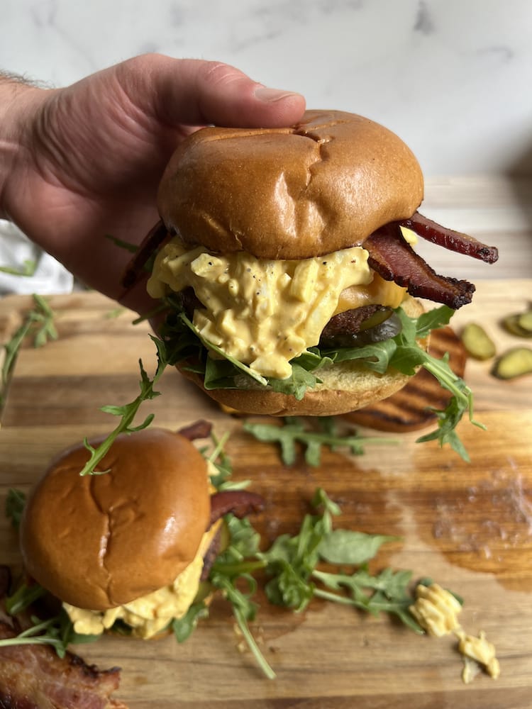 Sriracha Egg Salad Burger in a hand holding it above a cutting board and another burger