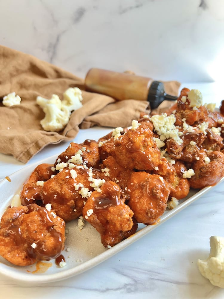Crispy Buffalo Cauliflower Bites on a serving plate garnished with bleu cheese and BBQ sauce