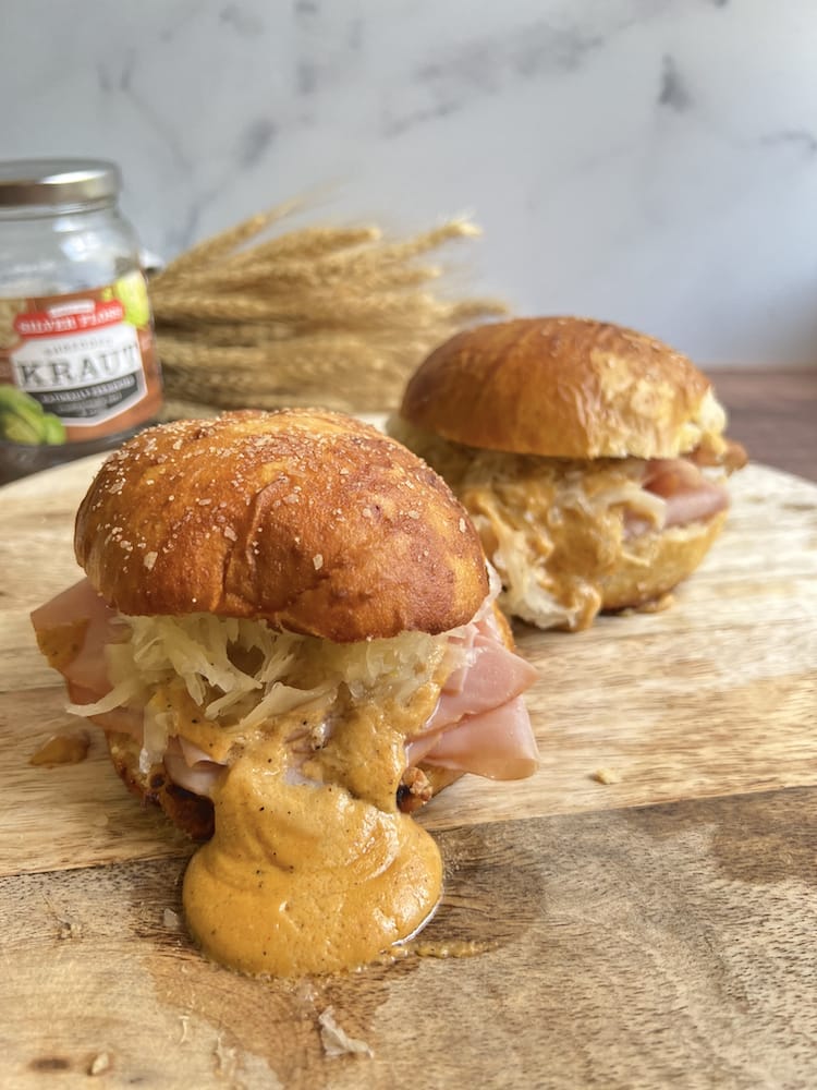 Hot Ham and Cheese Pretzel Sandwich on a cutting board with wheat and sauerkraut jar behind it
