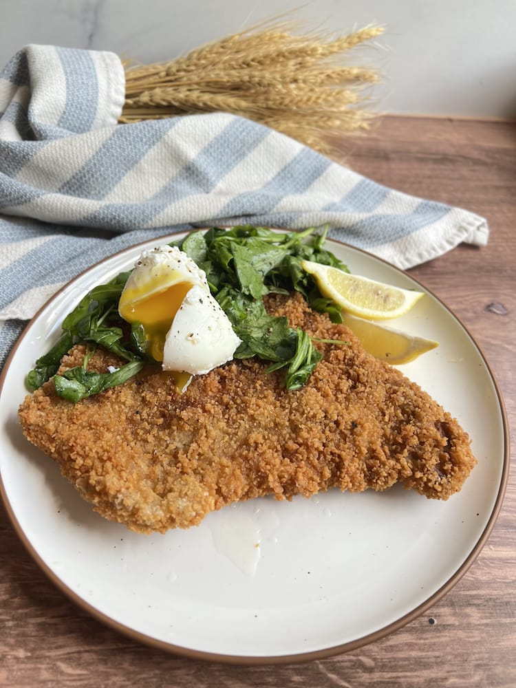 A Pork Tenderloin Schnitzel topped with arugula salad and a poached egg on a plate