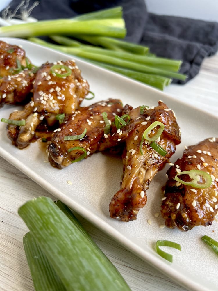 Chicken Wings with Chinese Plum Sauce on a white plate surrounded by fresh scallions