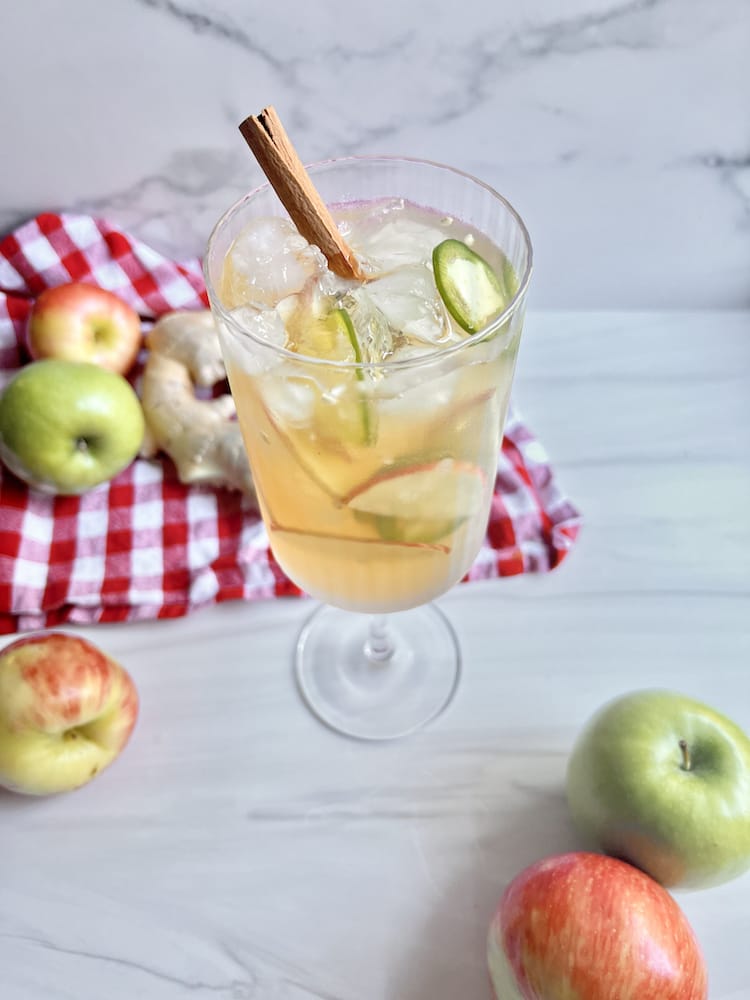 Mulled Cider Sangria in a large stemmed wine glass surrounded by apples