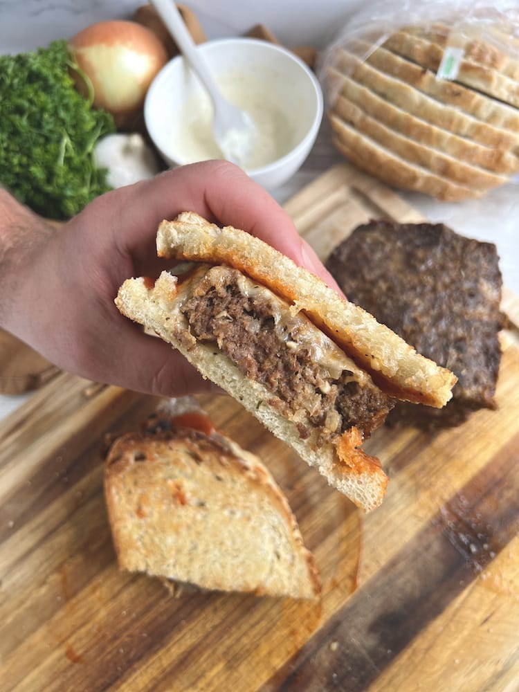 Hangry Meatloaf Sandwich held in a hand above meatloaf, garlic aioli, and bread on a cutting board