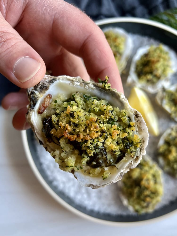 A hand holding pme o the Oysters on the Half Shell plated below