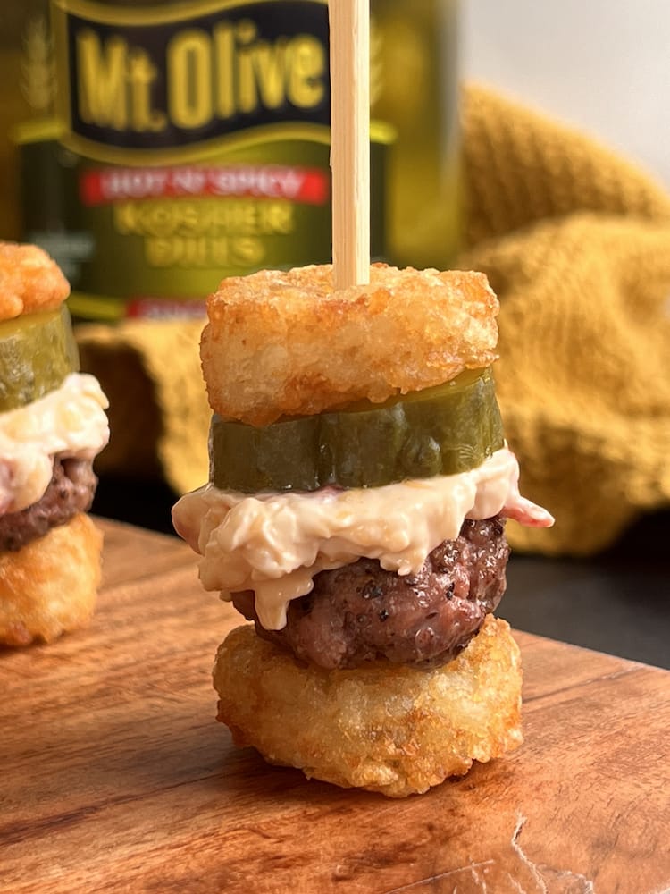 Pimento Cheese Burger Bites on a cutting board with a jar of pickles in the background