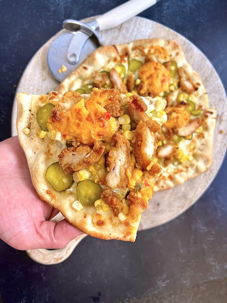 A slice of Souther-Style Pickle Pizza held by a hand over the rest of the pizza pie