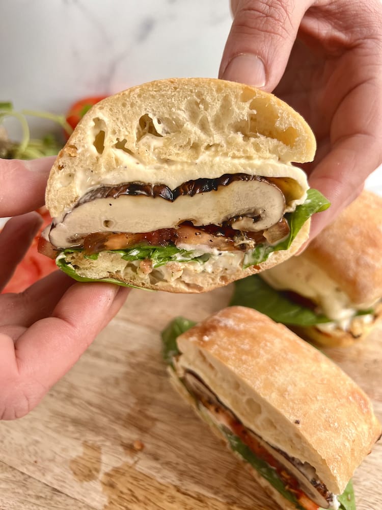 Two hands holding a Caprese Portobello Sandwich that's been cut in half