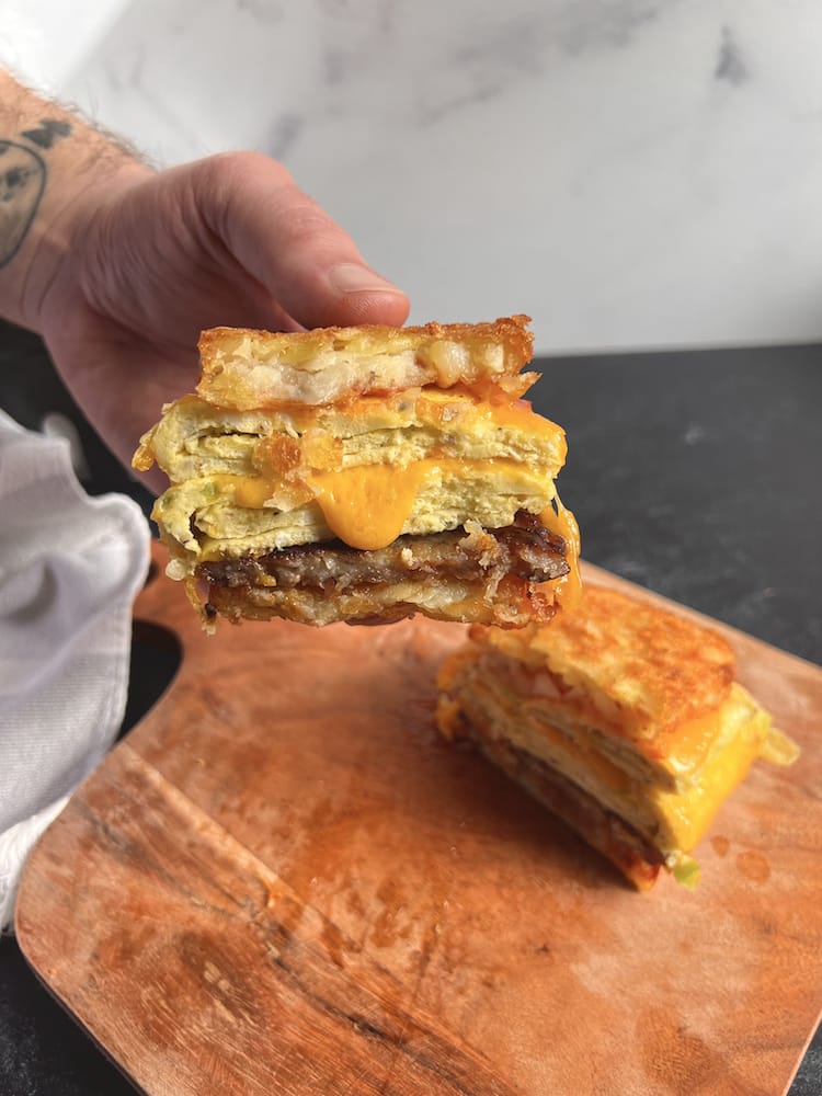 Sausage and Egg Hashbrown Sandwich cut in half with one half held by a hand toward the camera