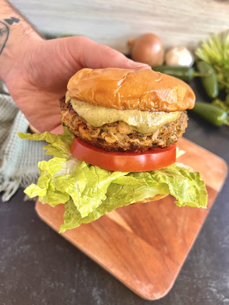 Cilantro Lime Salmon Burger held in a hand above a wooden cutting board