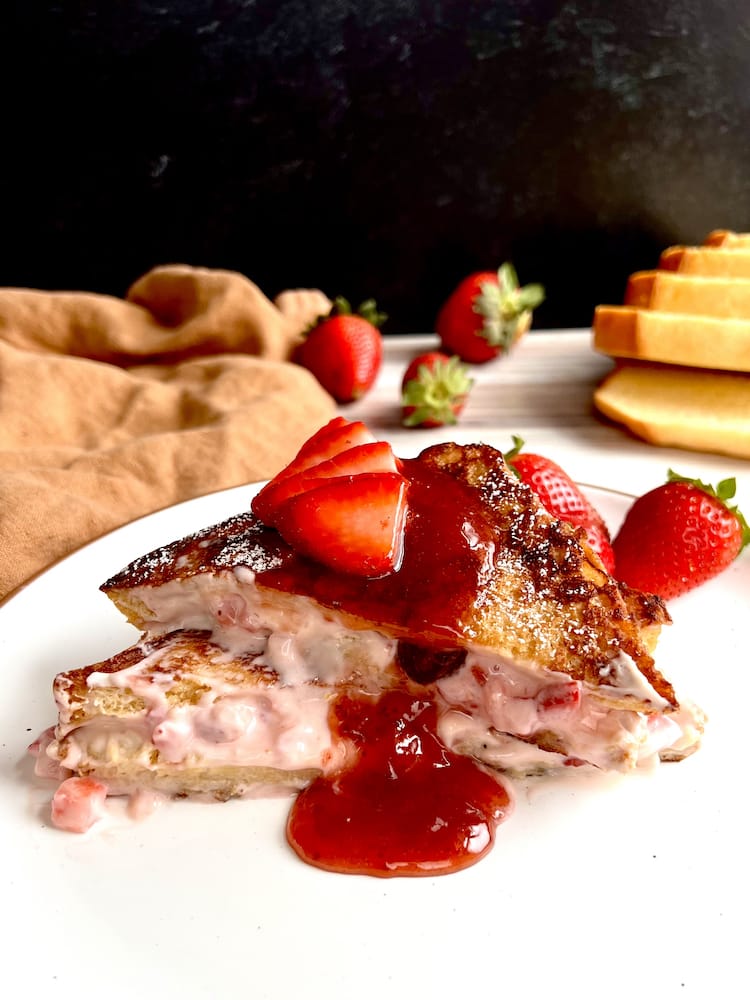 Strawberry Stuffed French Toast on a white plate with fresh strawberries and sliced brioche bread in the background