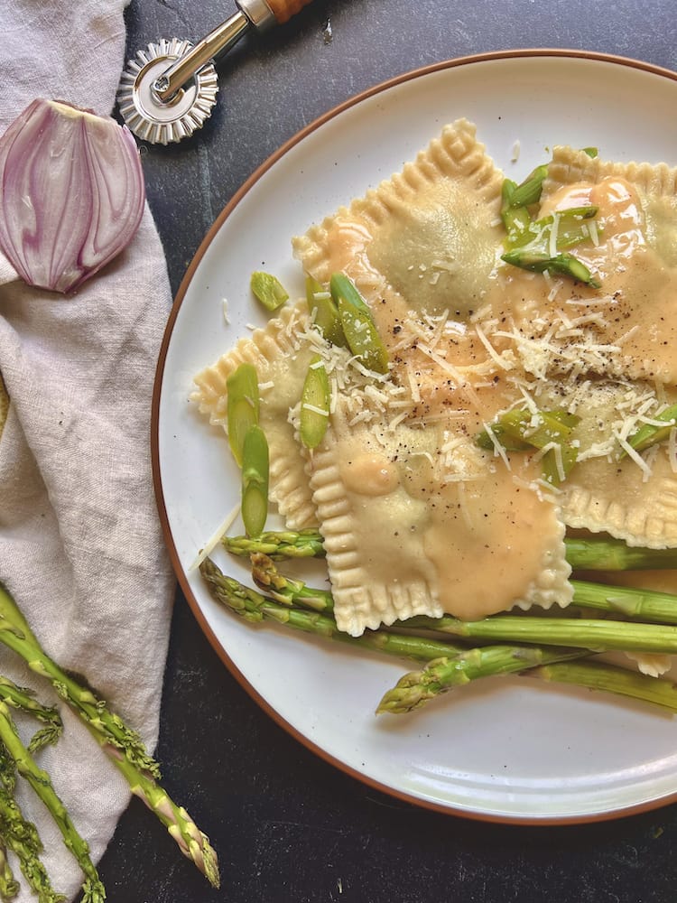 Asparagus Ravioli with Lemon Beurre Blanc on a plate with blanched asparagus