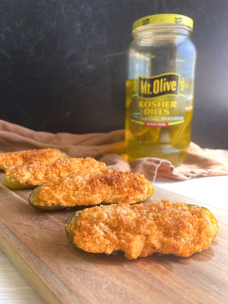 Buffalo Chicken Pickle Poppers on a wooden cutting board with a jar of pickles in the background