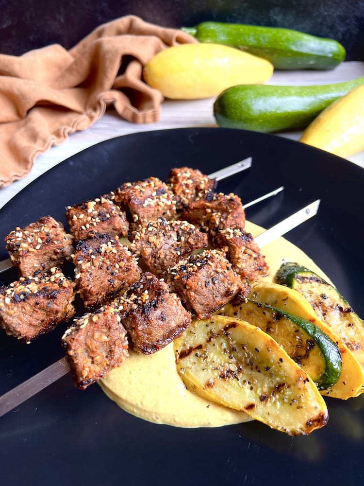 Beef Kebabs with Curry Yogurt Sauce on a black plate with grilled summer squash and zucchini